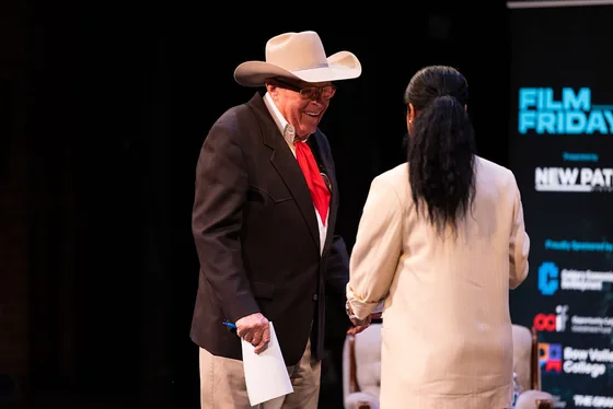 A smiling guest in a cowboy hat talking with the host on stage.